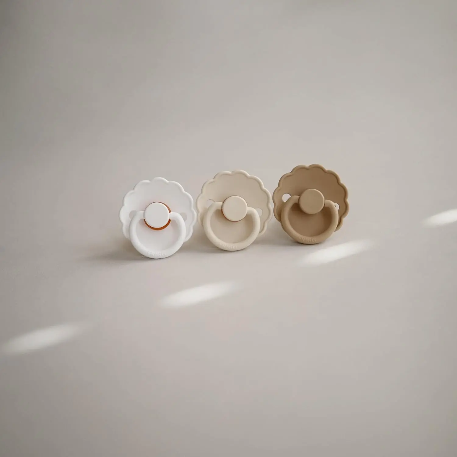 Two-pack of FRIGG Daisy pacifiers in baked clay and cream colors, size 2, designed for babies 6-18 months and made with SilkySoft medical grade silicone.