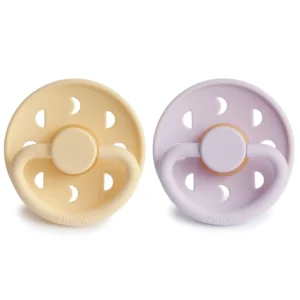 Two FRIGG Moon Phase natural rubber pacifiers in pale daffodil and soft lilac colors, designed with a cherry-shaped nipple and made without BPA for babies aged 0-6 months.